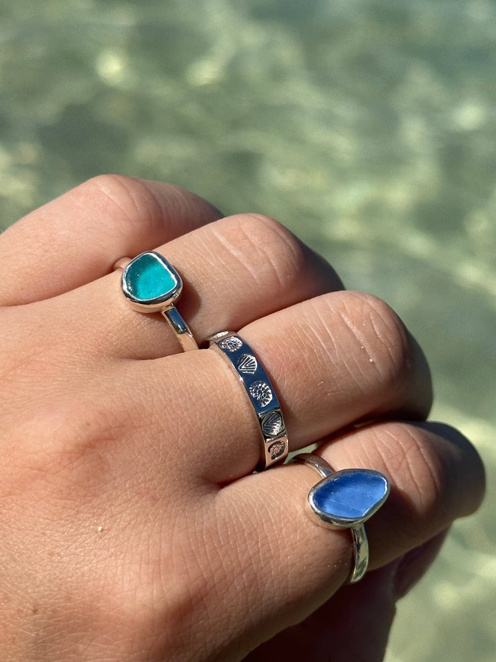 Hand wearing two rings with turquoise and blue stones against a blurred natural background