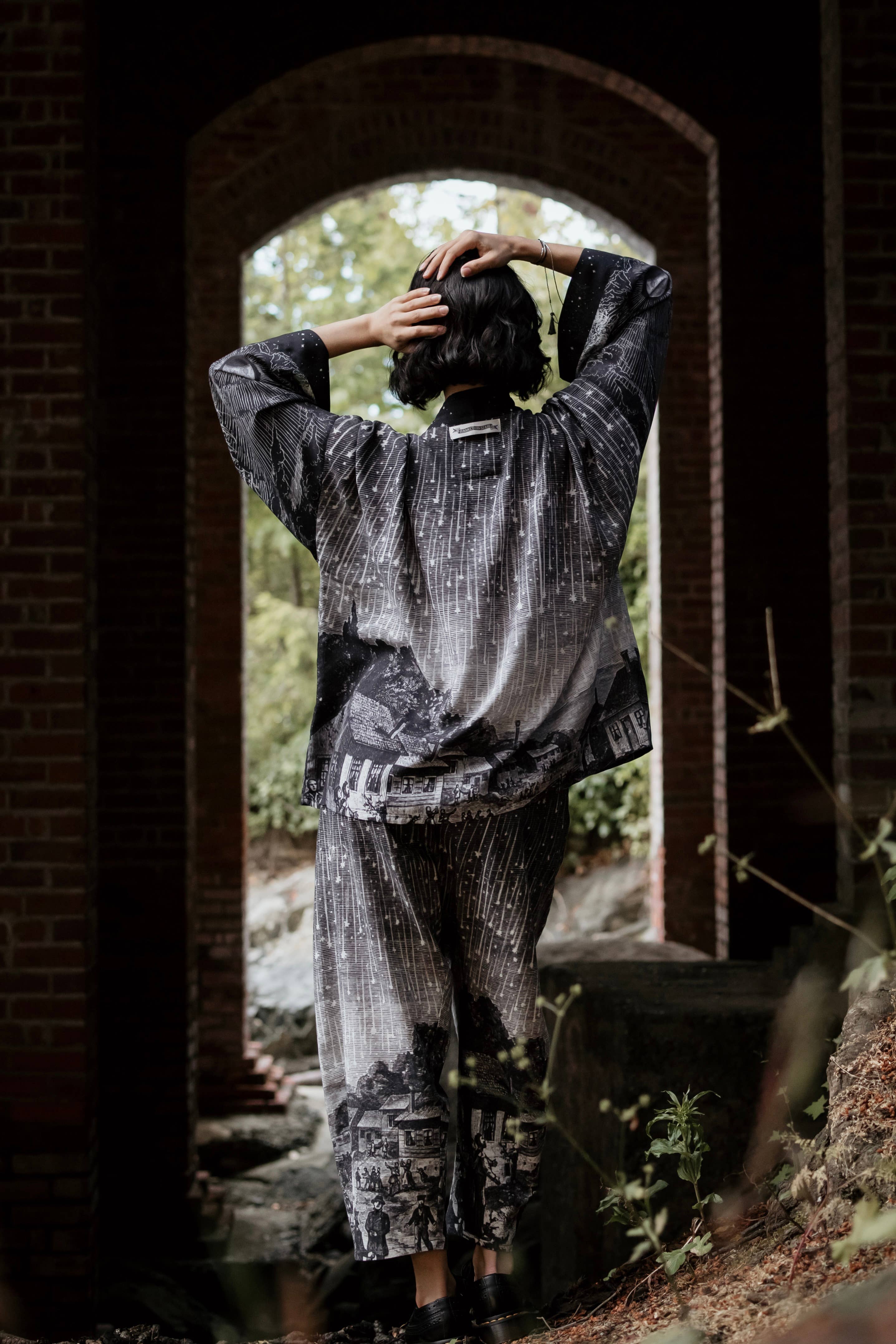 Person wearing a patterned outfit standing in an archway with a natural background