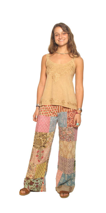 Woman wearing a beige sleeveless top and colorful patchwork pants on a white background