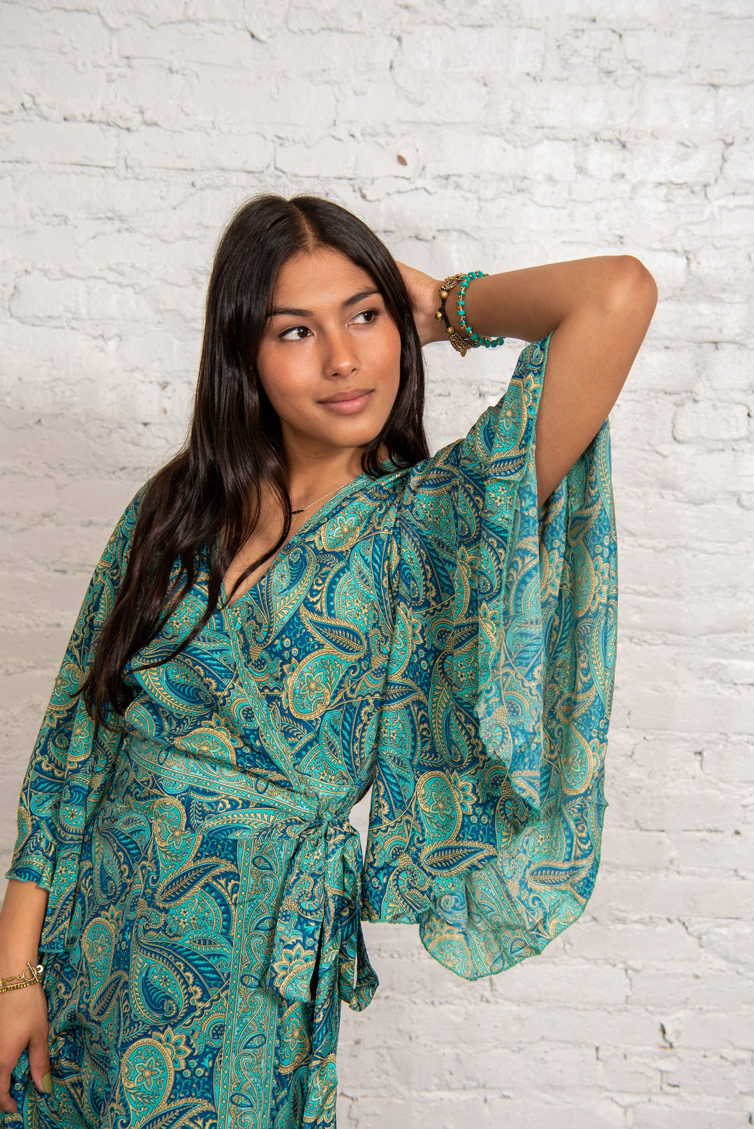 Woman wearing a teal patterned dress against a white brick wall