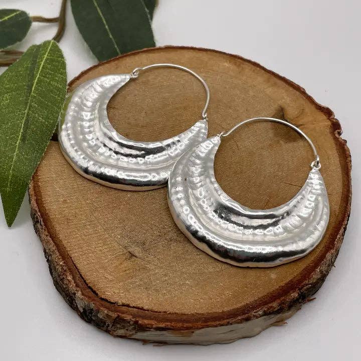 Silver hoop earrings on a wooden surface with leaves in the background