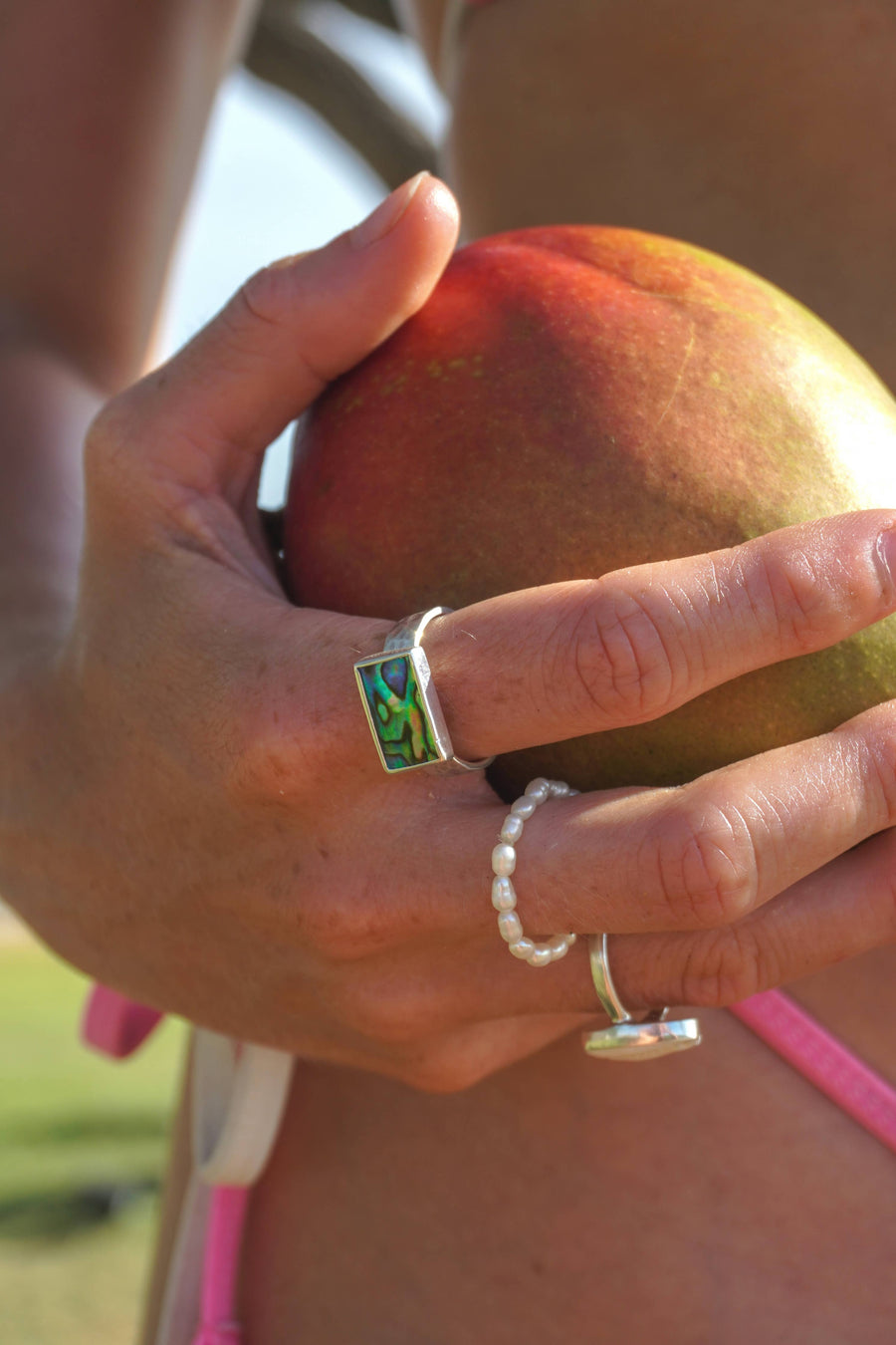 Hand holding a mango with multiple rings on a blurred natural background