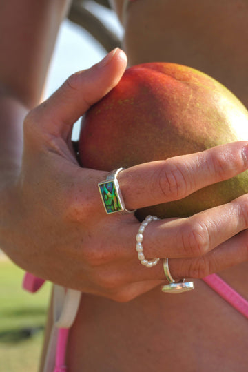 Hand holding a mango with multiple rings on a blurred natural background