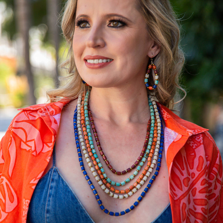 Woman wearing a colorful outfit with a red jacket and blue top, standing outdoors.