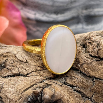 Gold ring with a white stone on a wooden surface