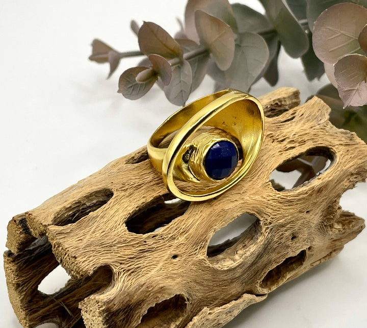 Gold ring with a blue stone on a piece of driftwood with flowers in the background