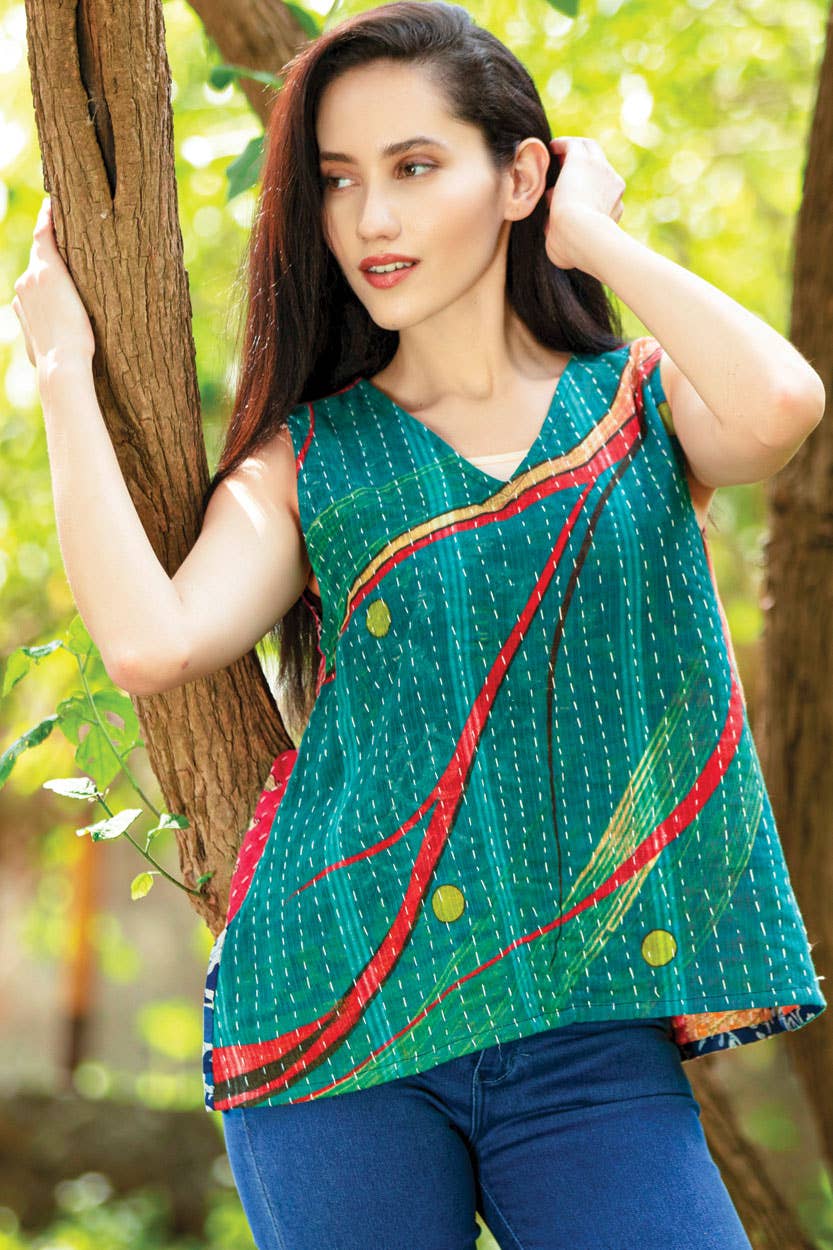 Woman wearing a green sleeveless top with red and yellow patterns, standing outdoors with trees in the background.