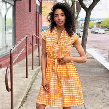 Woman in a yellow checkered dress standing on a sidewalk.
