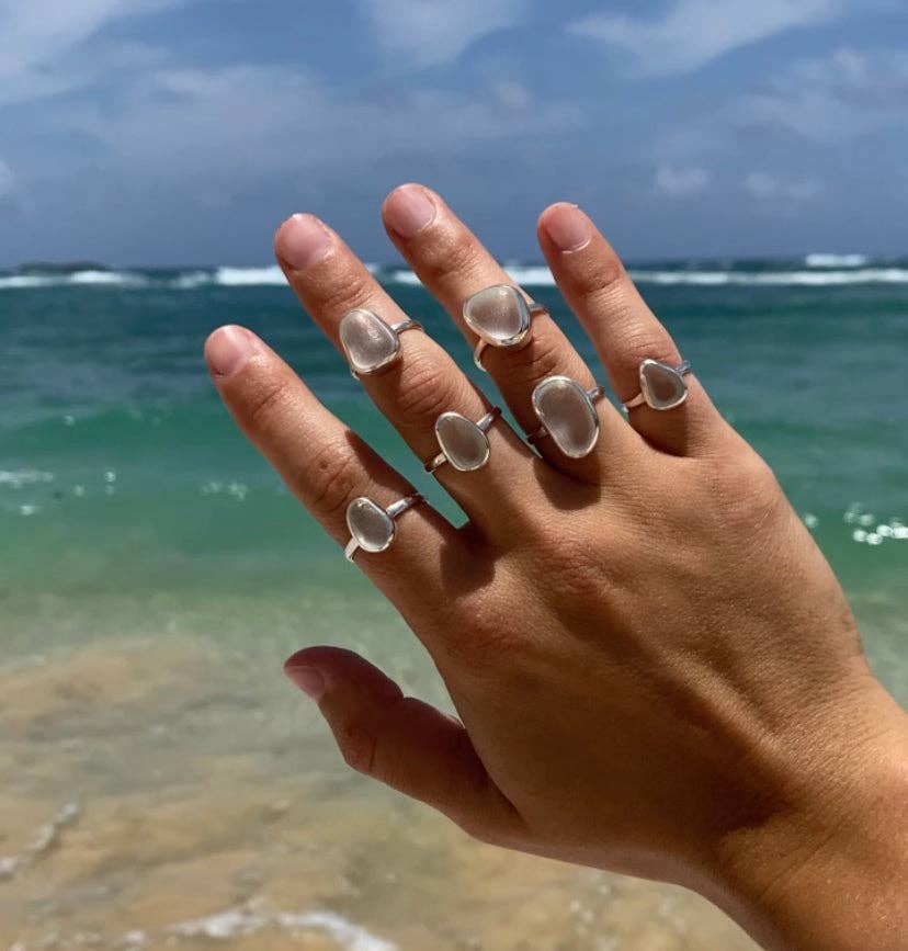Hand wearing multiple clear stone rings with ocean and sky in the background