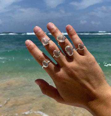 Hand wearing multiple clear stone rings with ocean and sky in the background