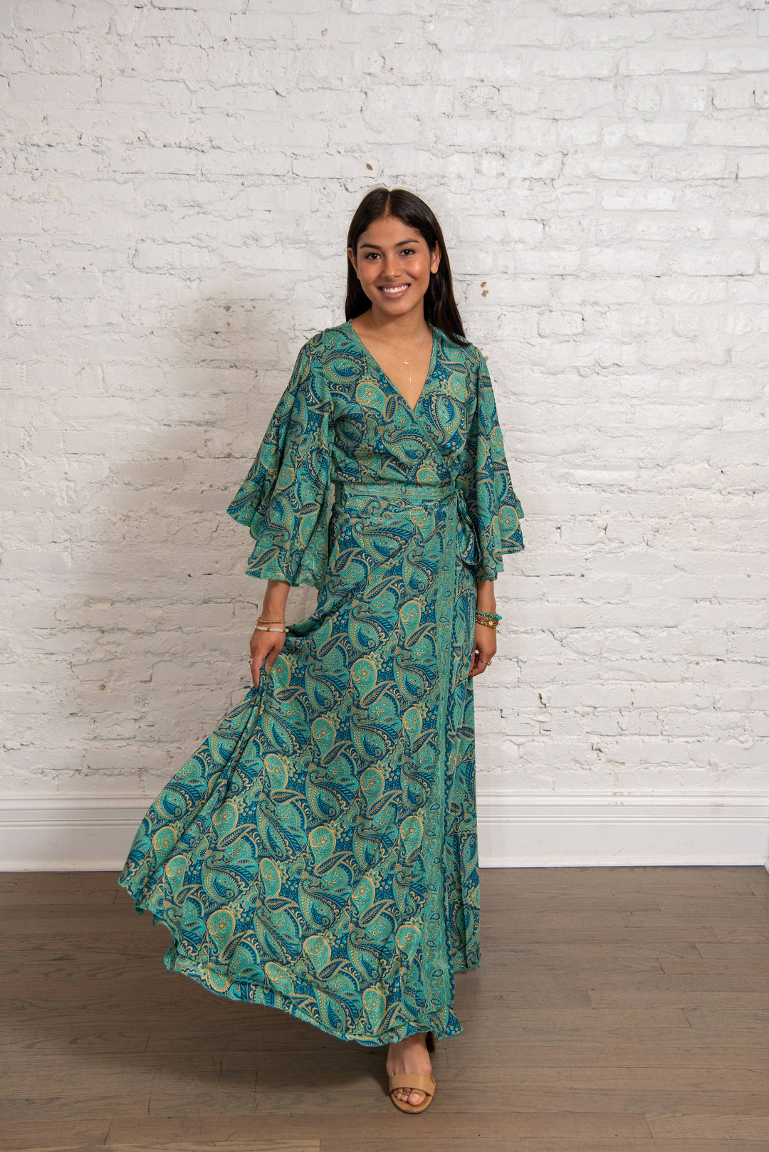 Woman wearing a green patterned dress standing against a white brick wall.