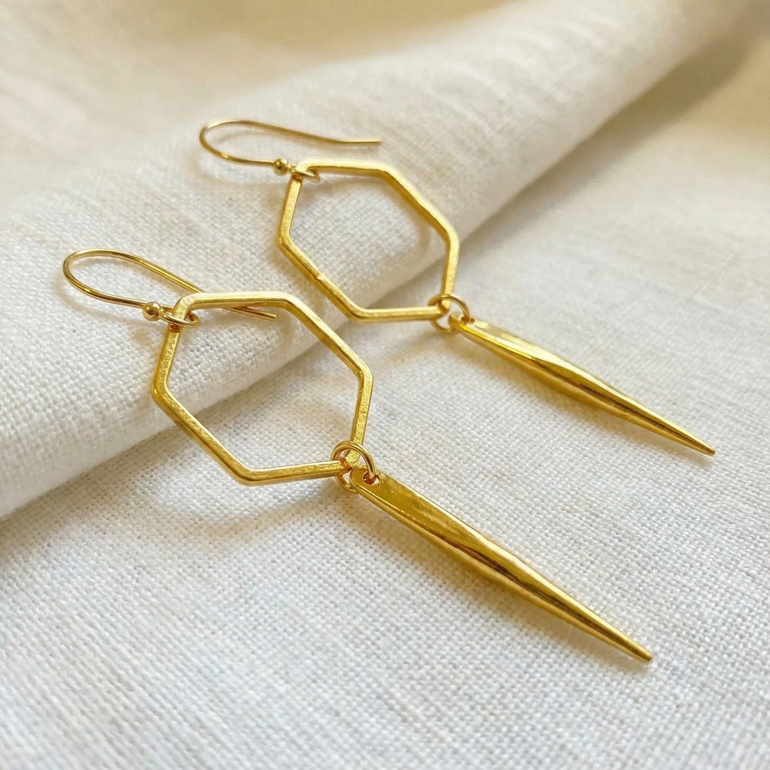 Gold geometric earrings on a textured beige surface