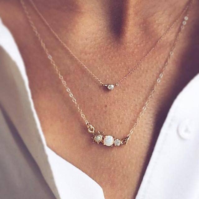 Close-up of a person wearing two delicate necklaces with small stones on a blurred background.