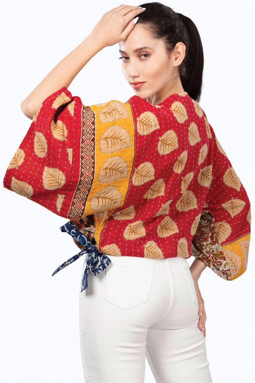 Woman wearing a red and yellow patterned top with white pants on a white background