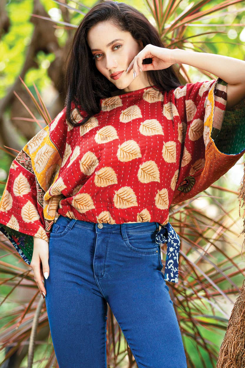 Woman wearing a red patterned top and blue jeans standing in a natural setting.