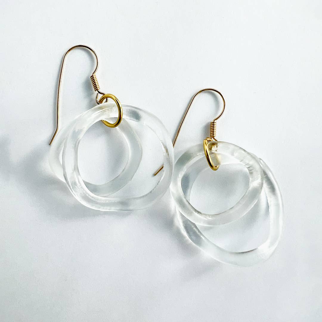 Clear circular earrings with gold hooks on a light gray background