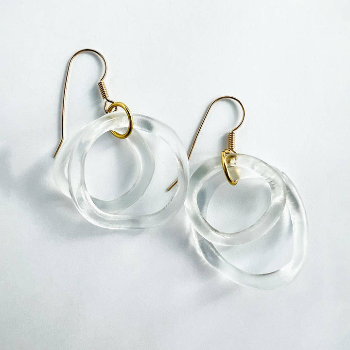 Clear circular earrings with gold hooks on a light gray background