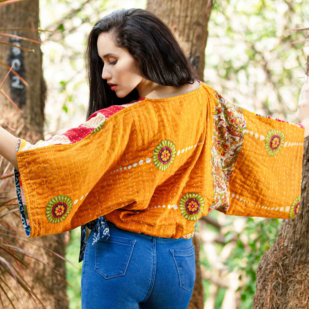 Woman wearing a bright orange traditional garment with floral patterns in a natural setting.