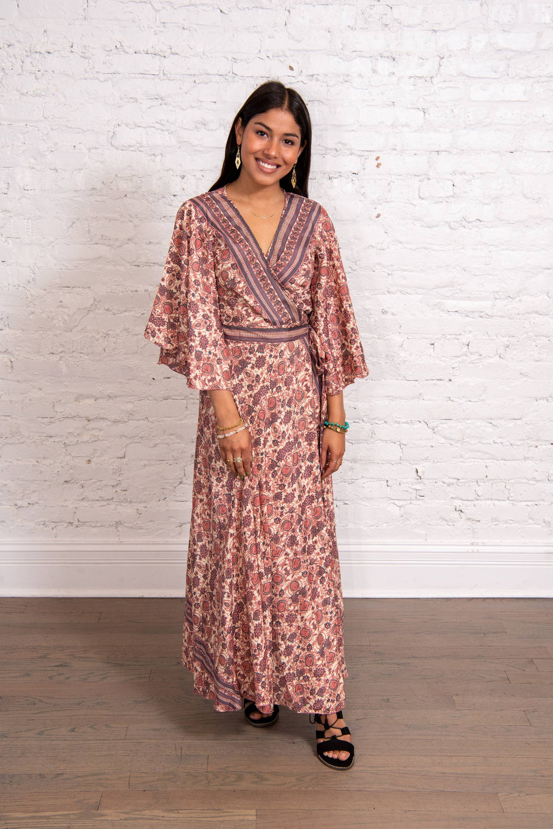 Woman wearing a floral dress against a white brick wall.