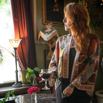 Woman standing in a room with a window, curtains, and decorative items.