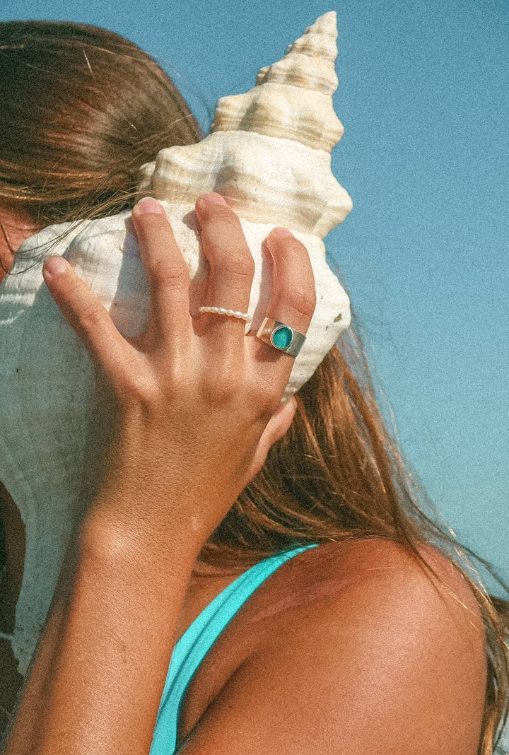 Person holding a large shell to their ear with a clear blue sky background