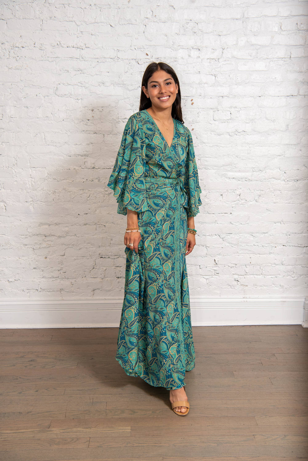 Woman wearing a green patterned dress standing against a white brick wall.