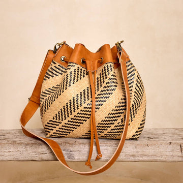 Rattan sling bag with black and ivory plaid weave and black leather trim, handwoven by Dayak artisans of Borneo