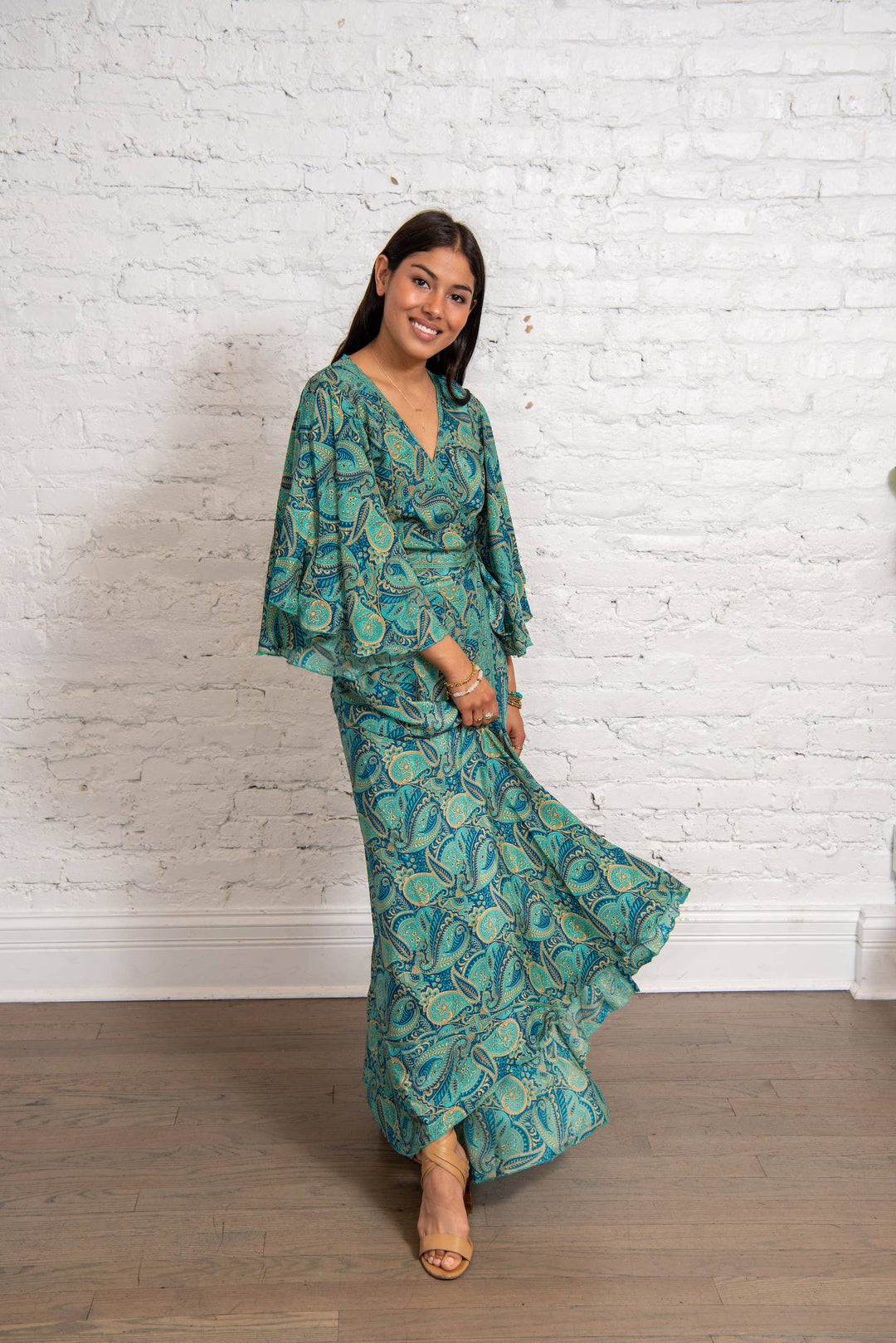 Woman wearing a green patterned dress against a white brick wall.