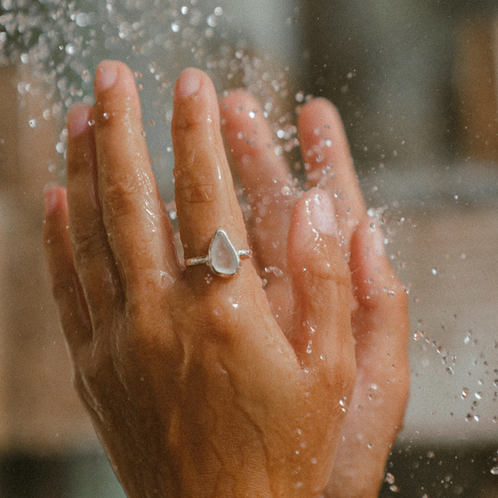 Hand with a ring holding water droplets against a blurred background