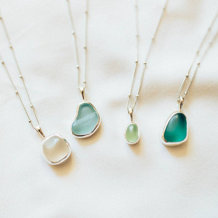 Four necklaces with green pendant stones on a white background