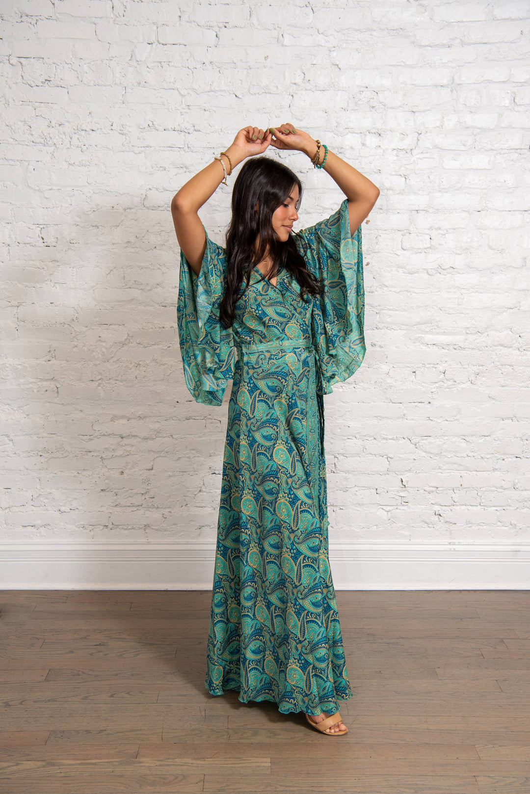 Woman wearing a green patterned dress against a white brick wall.
