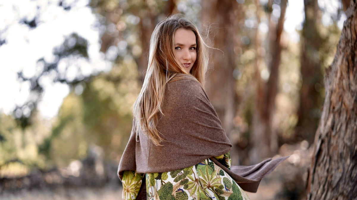 A woman in a forest setting, wearing a brown shawl draped over her shoulders and a green botanical print skirt.