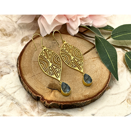 Gold earrings with leaf designs on a wooden slice with flowers and leaves.