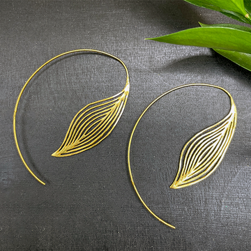 Gold leaf-shaped earrings on a dark fabric background with green leaves.