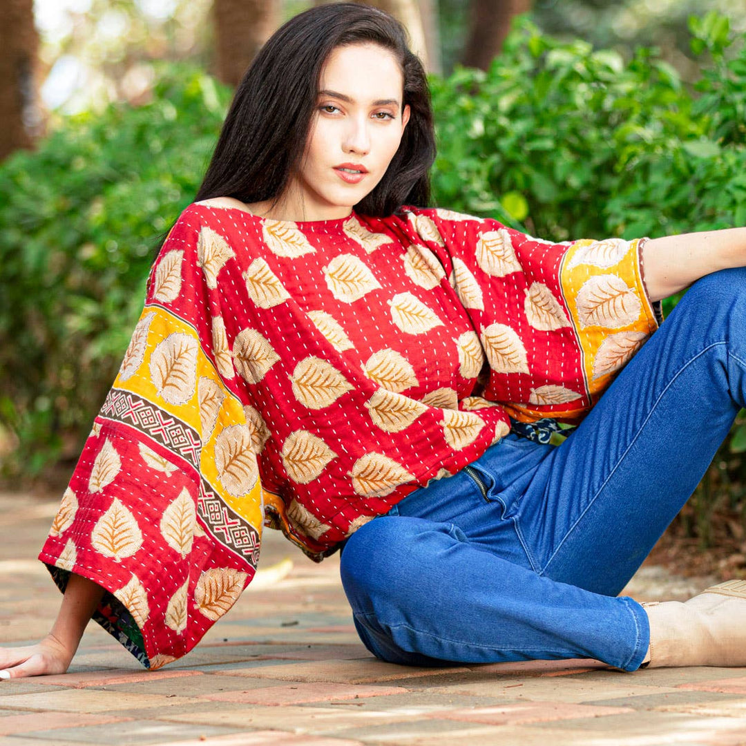 Woman wearing a red patterned top and blue jeans sitting outdoors.