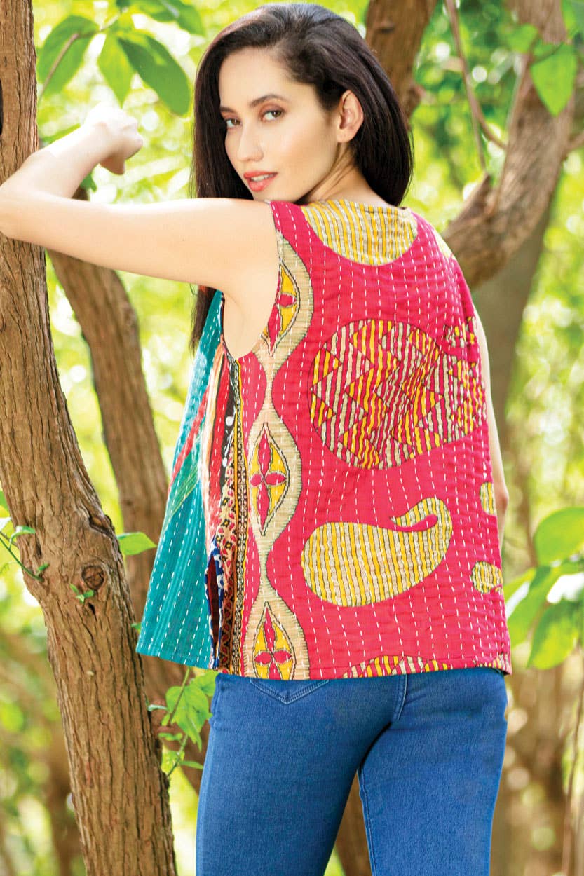 Woman wearing a colorful patterned top and blue pants standing in a natural setting.