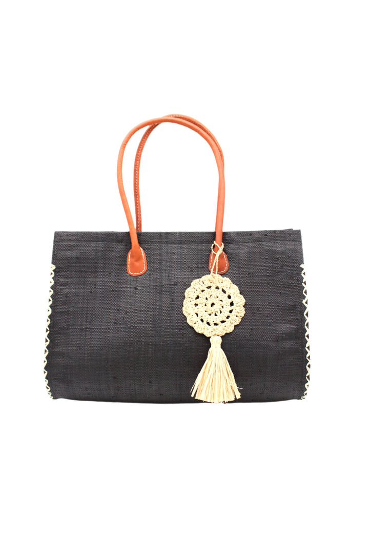 Black handbag with orange handles and a decorative tassel on a white background