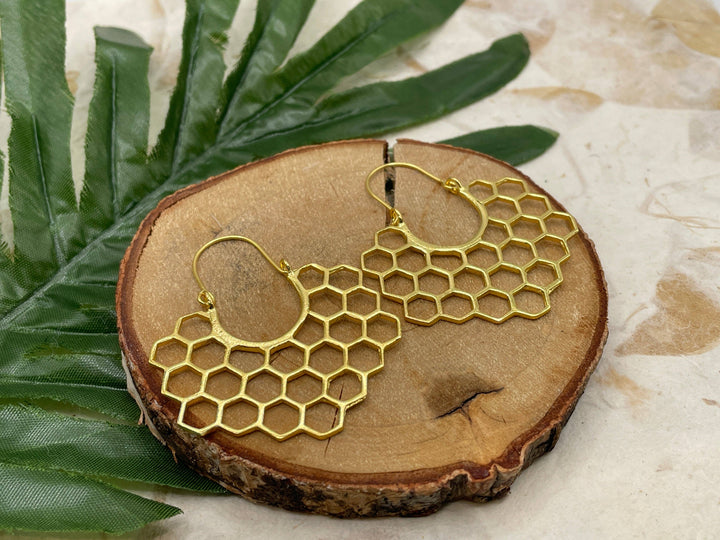 Gold honeycomb pattern earrings on a wooden surface with a leaf background