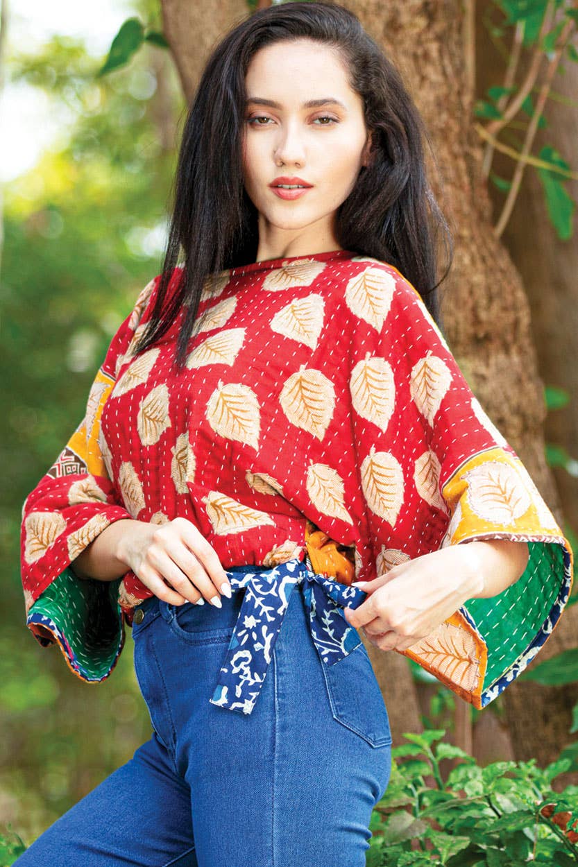 Woman wearing a red patterned top with blue jeans in a natural setting