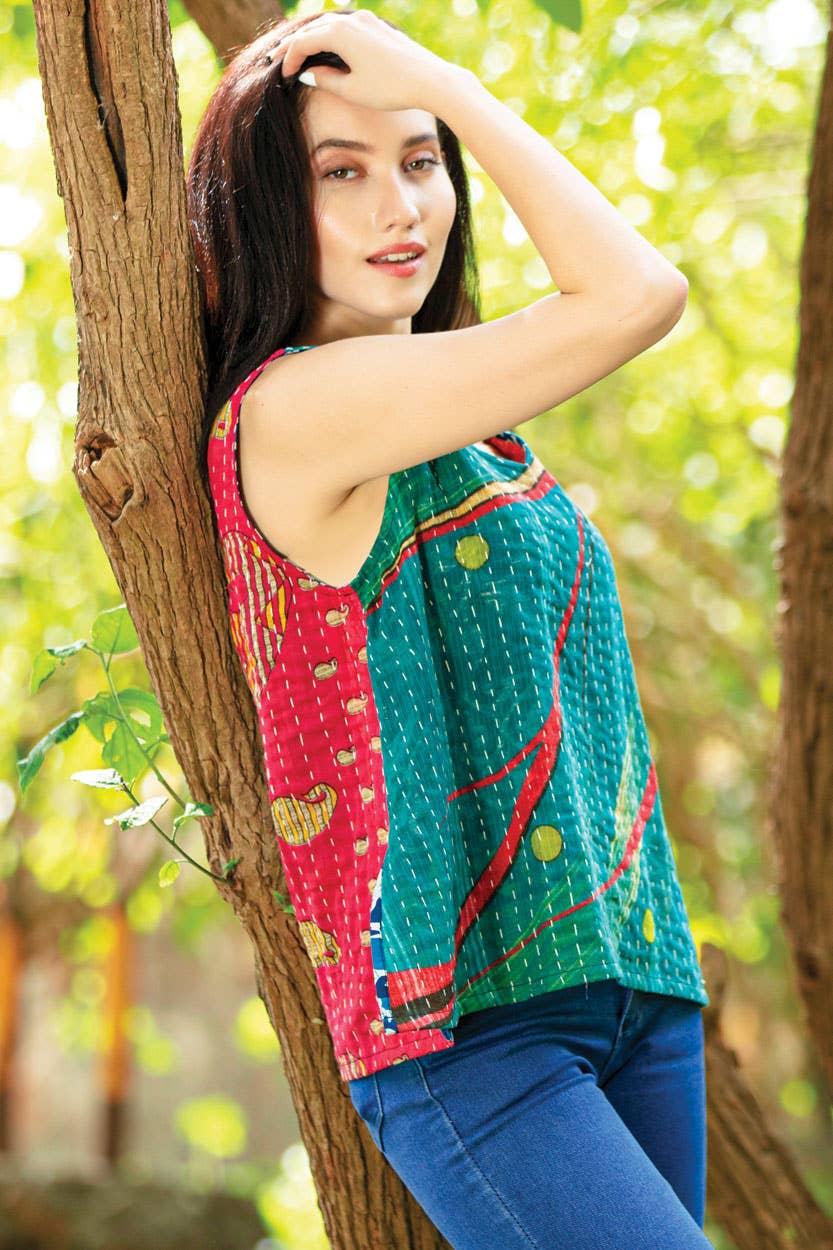 Woman in a colorful top and blue pants leaning against a tree in a natural setting