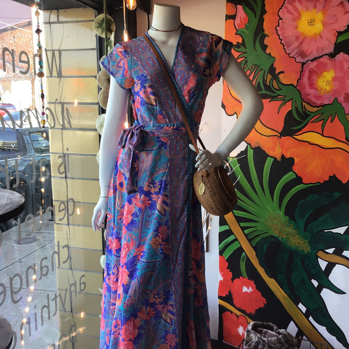 Mannequin wearing a colorful floral dress with a handbag in front of a vibrant floral mural.