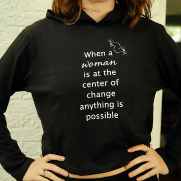 A person wearing a black cropped hoodie with text and a dragonfly symbol on it.