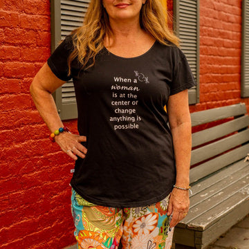 A woman wearing a black cotton scoop neck T-shirt with text on it, standing in front of a red wall.