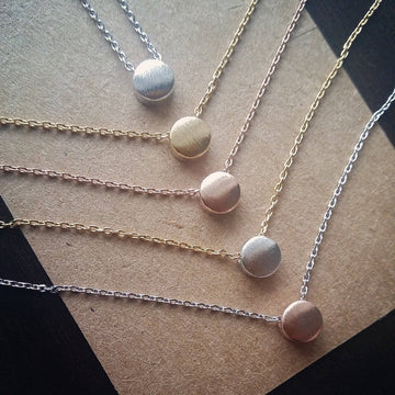 Five necklaces with round pendants on a textured surface