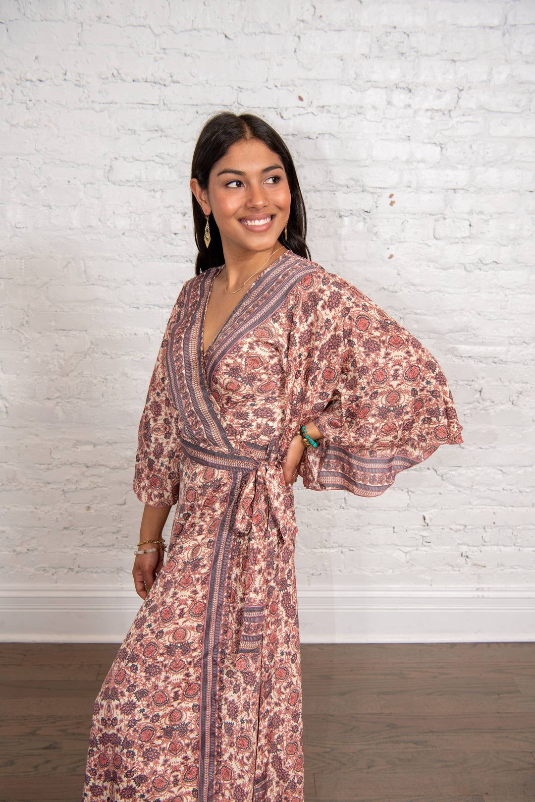 Woman wearing a floral dress against a white brick wall.