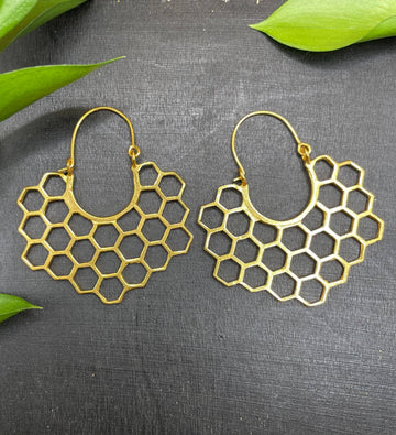 Gold honeycomb pattern earrings on a dark surface with green leaves.