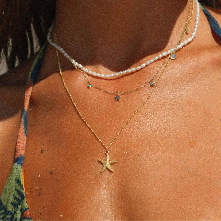 Close-up of a person wearing a gold starfish necklace and pearl necklace.
