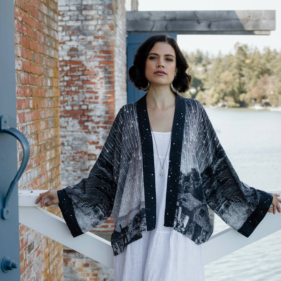 Woman wearing a black and white patterned kimono over a white dress by a lake.