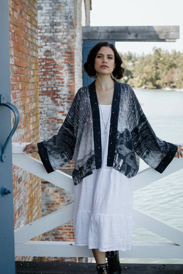 Woman wearing a black and white patterned kimono over a white dress by a lake.
