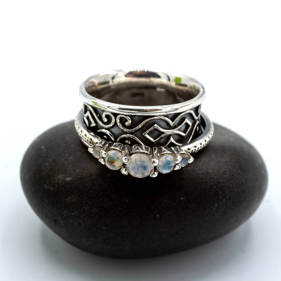 Silver ring with intricate design and gemstones on a black stone